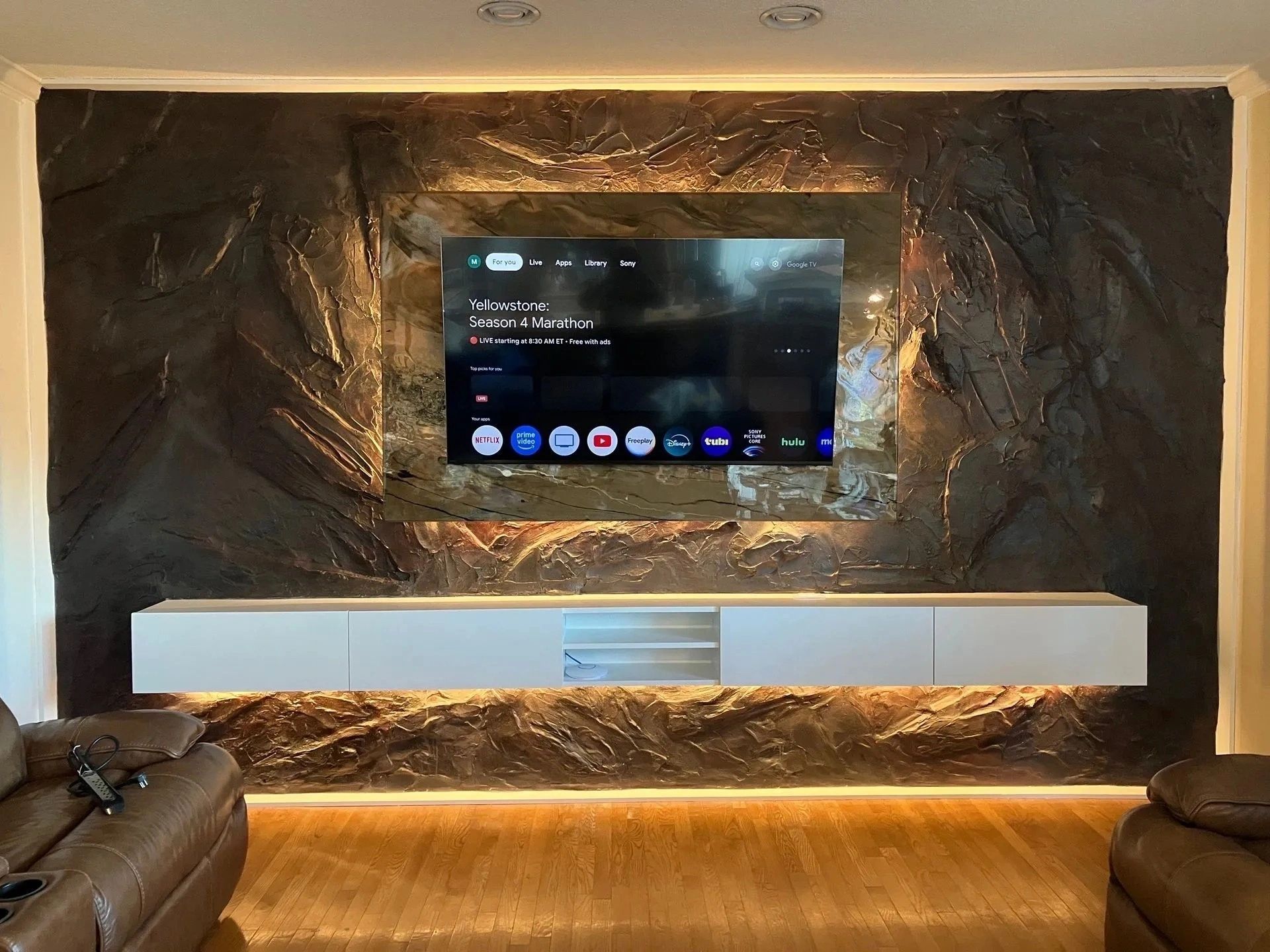 Modern living room with wall-mounted TV, stone accent wall, and warm under-shelf lighting