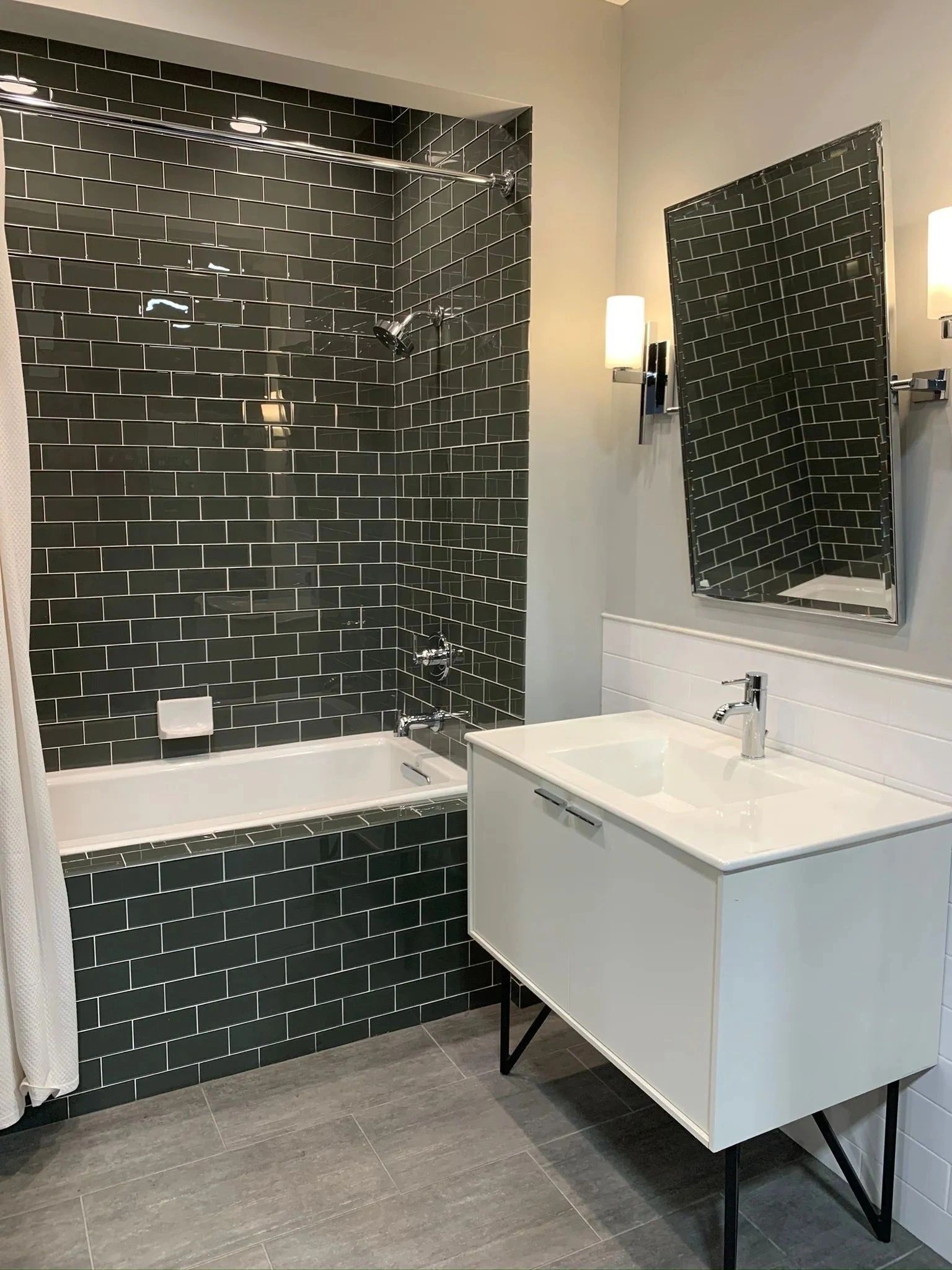 Modern bathroom with black tiled shower, white tub, and floating white vanity with mirror