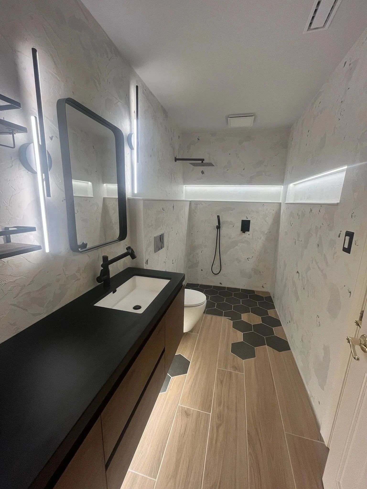 Modern bathroom with black vanity, white sink, large mirror, and marble-look walls and floor.