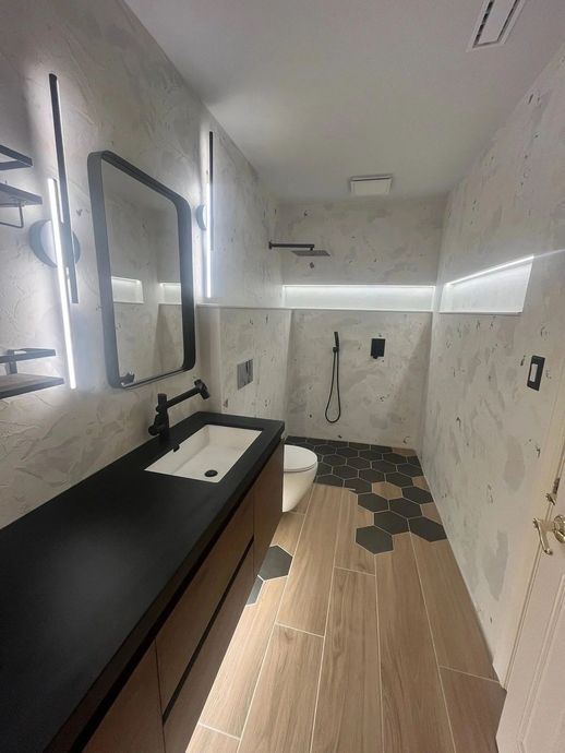 Modern bathroom with black vanity, white sink, large mirror, and marble-look walls and floor.