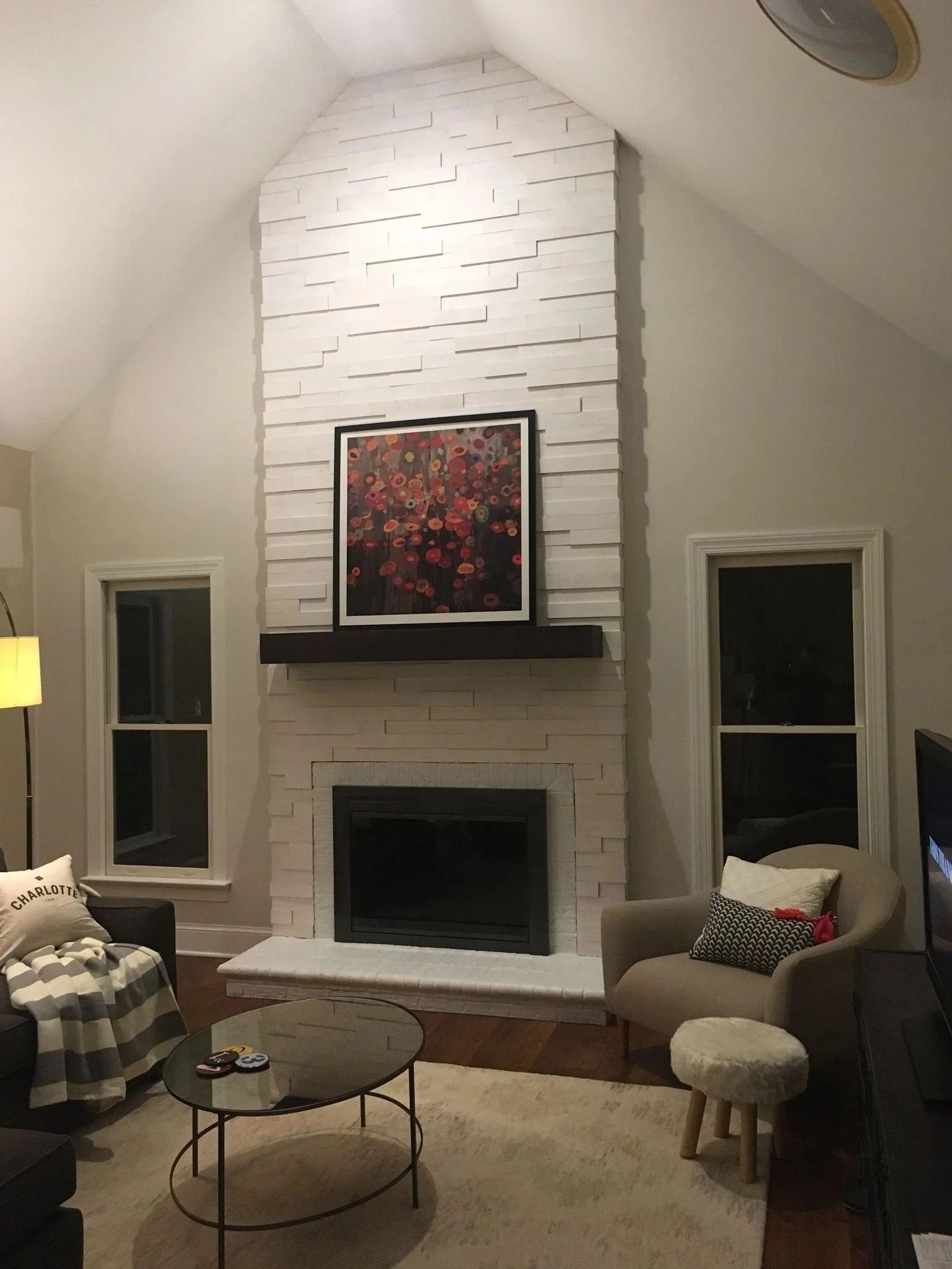 Cozy living room with white brick fireplace, vaulted ceiling, armchairs, and framed art above the mantel