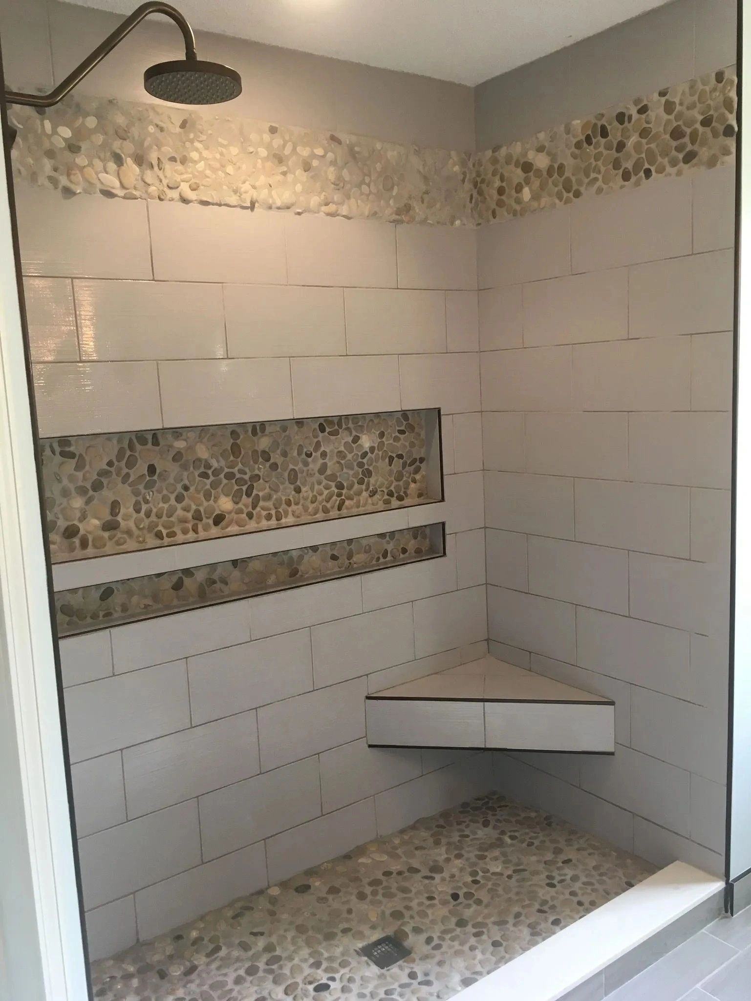 Tiled walk-in shower with bench, corner shelf, and showerhead, partially unfinished with exposed wall board.