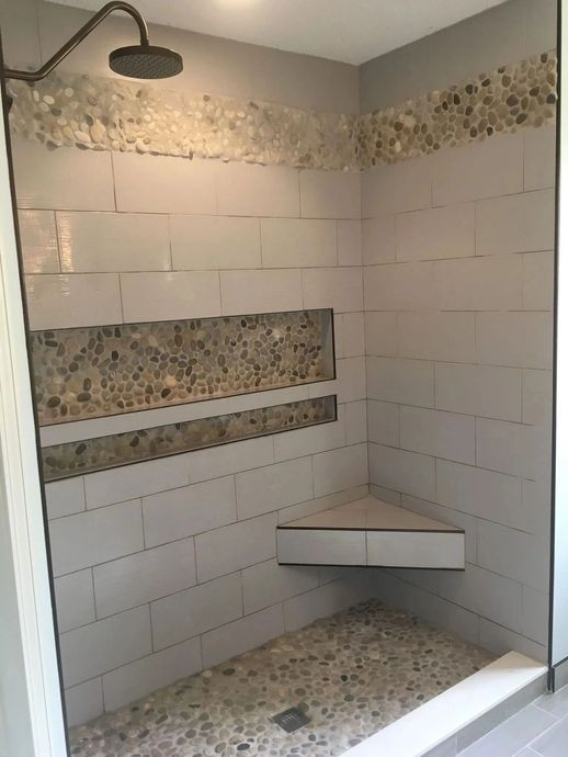 Tiled walk-in shower with bench, corner shelf, and showerhead, partially unfinished with exposed wall board.
