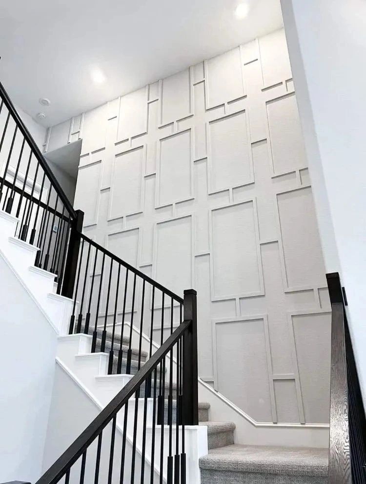 Staircase with black railing beside a white wall of decorative recessed panels