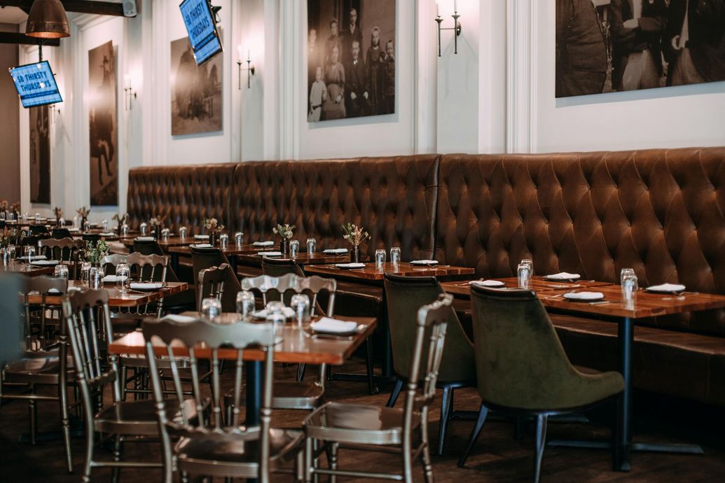 Empty restaurant interior with tufted brown banquette seating, wooden tables, and framed wall art