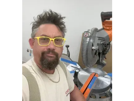 Person with yellow glasses next to a miter saw in a workshop