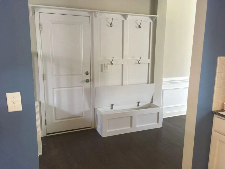 White mudroom with built-in bench and hooks beside a closed door, dark wood floor, and blue walls