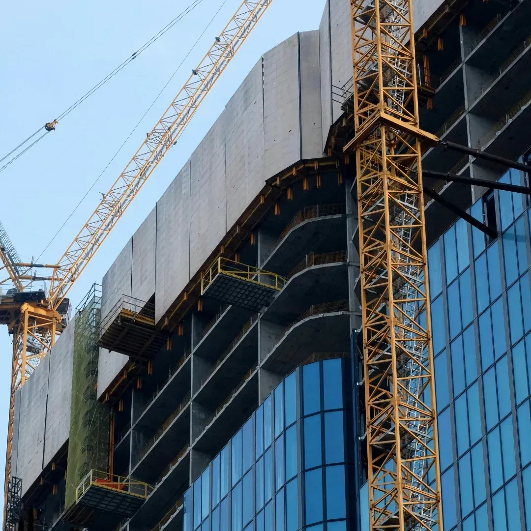 High-rise building under construction with cranes and reflective blue glass facade High-rise building under construction with cranes and reflective blue glass facade