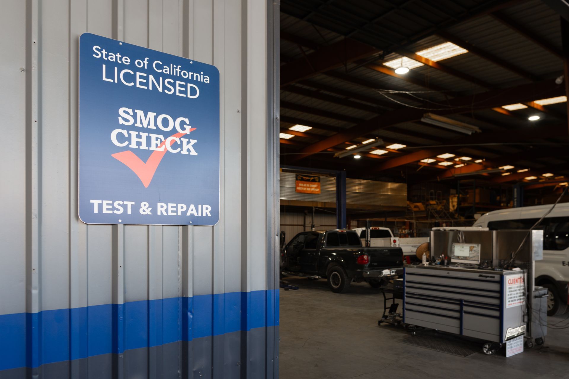 Sign for a licensed smog check at a California auto repair shop, blue and white text on a metal building.