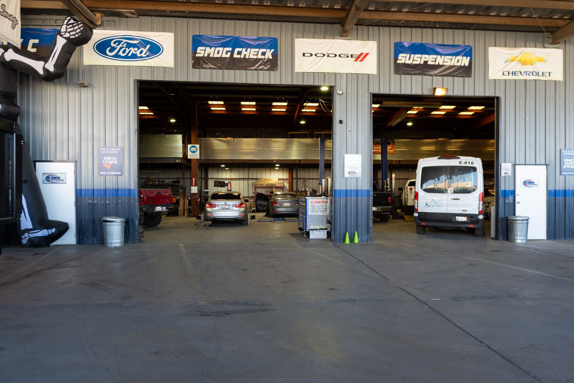 Auto repair shop with open bays, cars inside, and banners for Ford, Dodge, and Chevy.
