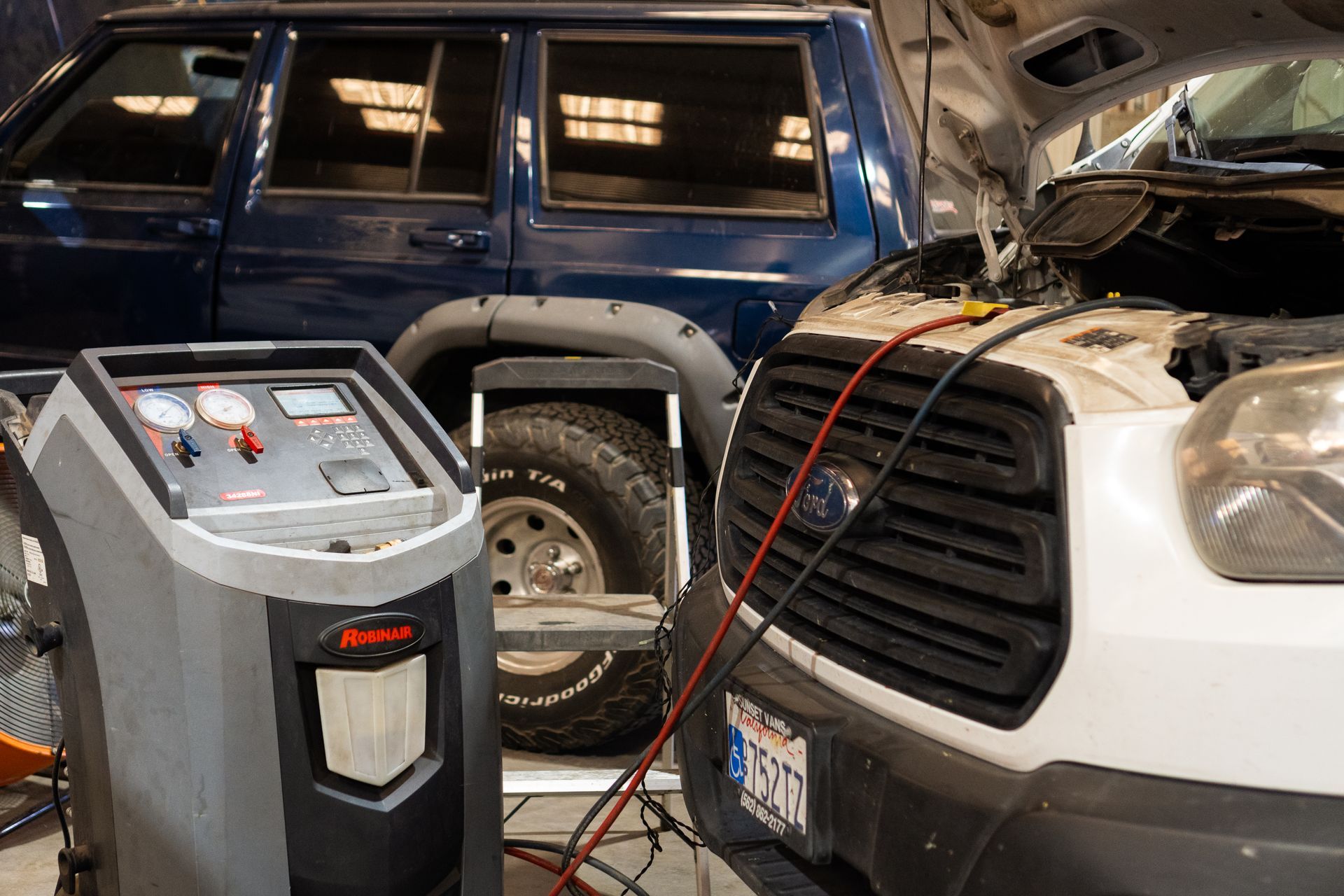 Battery charger connected to a white vehicle in a garage, with a blue SUV in the background.