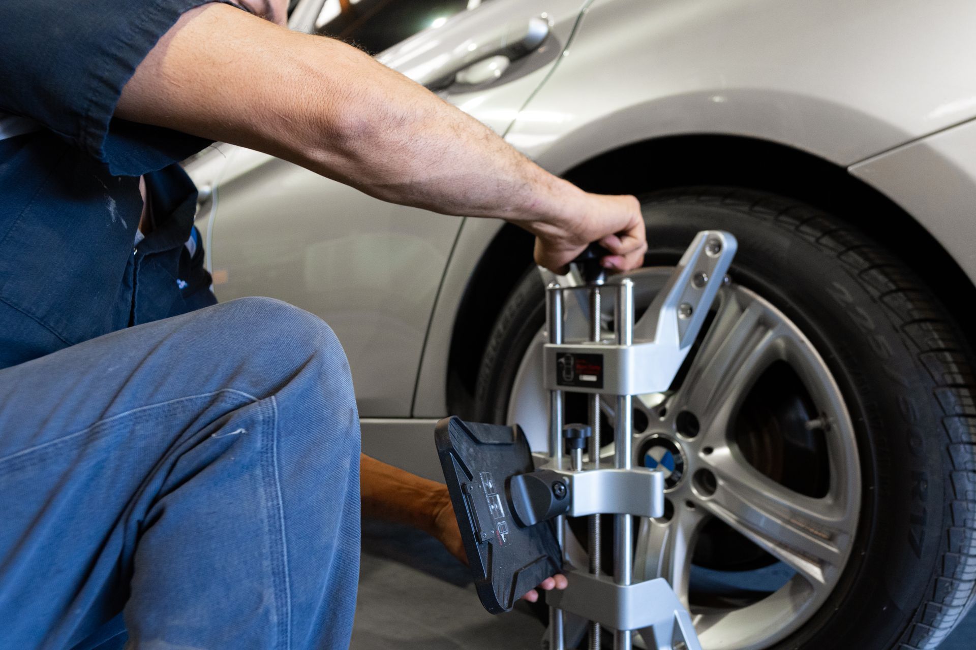 Mechanic adjusting car wheel alignment tool on a silver car tire.