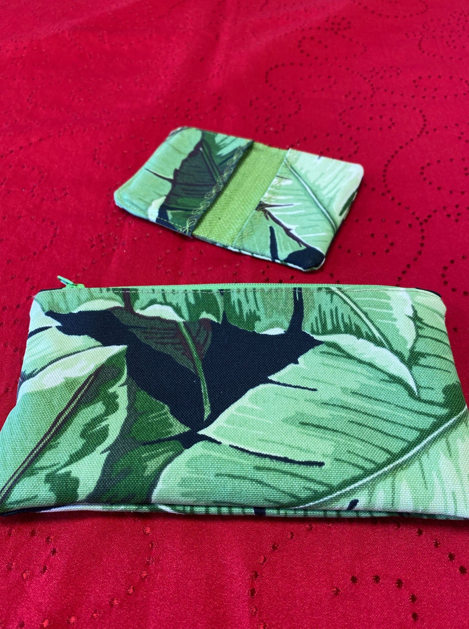 Two green leaf-patterned fabric pouches on a red textured surface