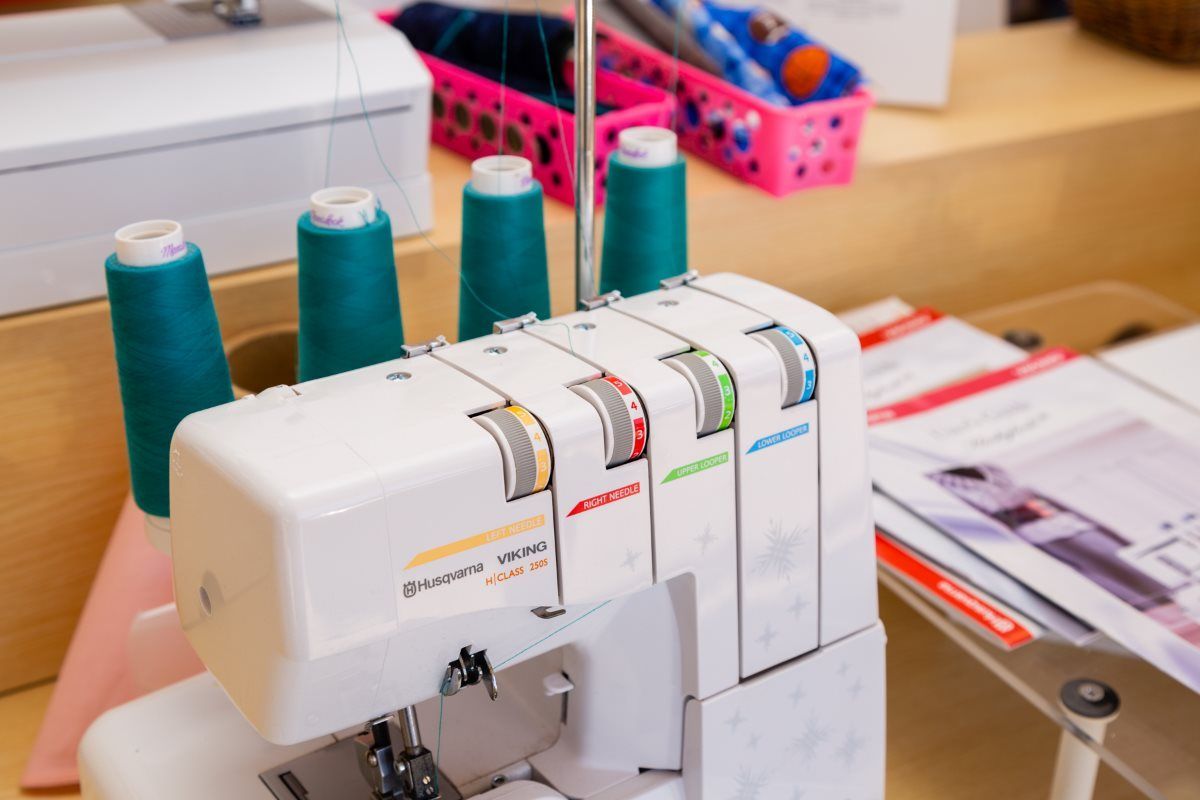 White serger sewing machine with teal thread spools on a craft table