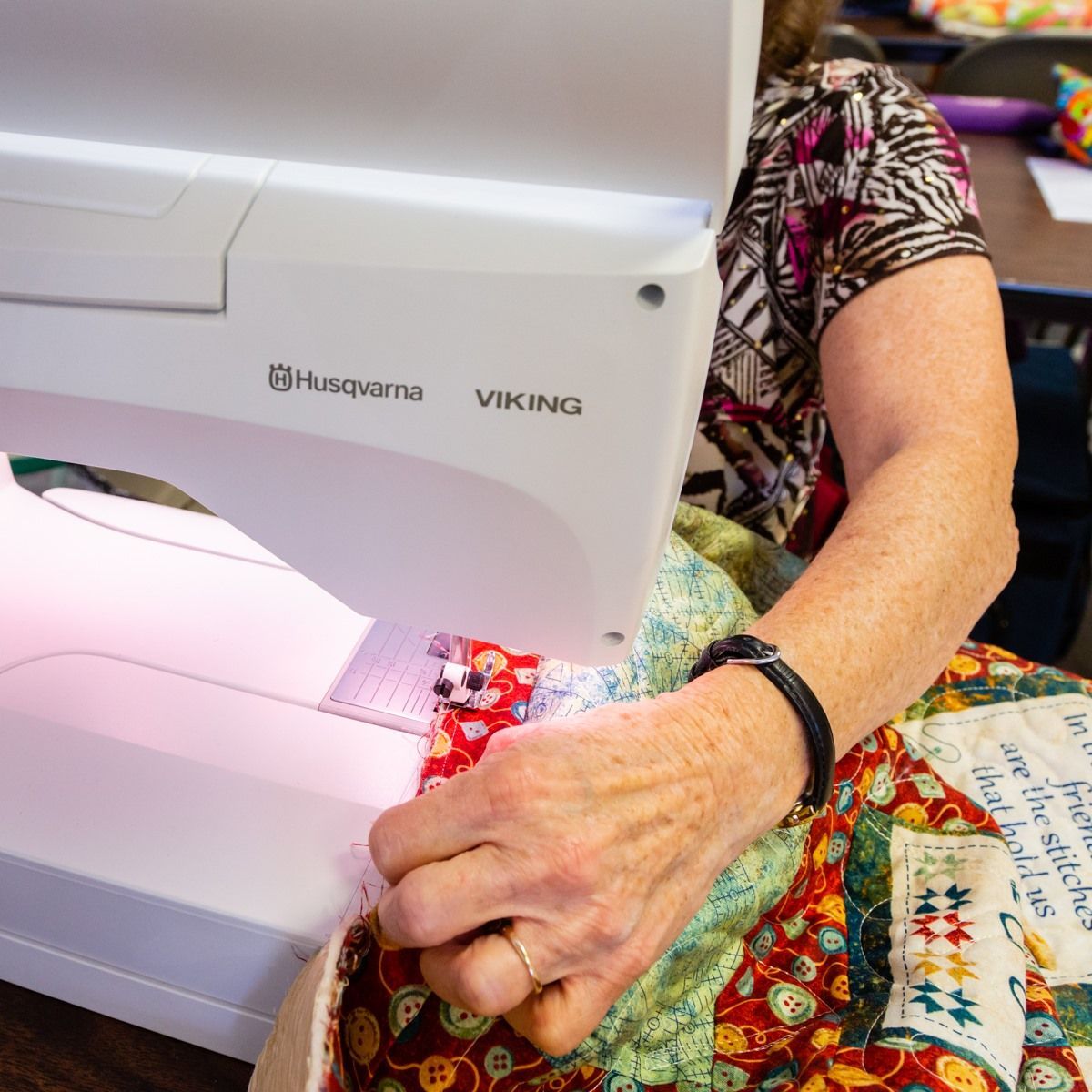 Woman sewing colorful fabric on a Husqvarna Viking machine, close-up of hands and needle area