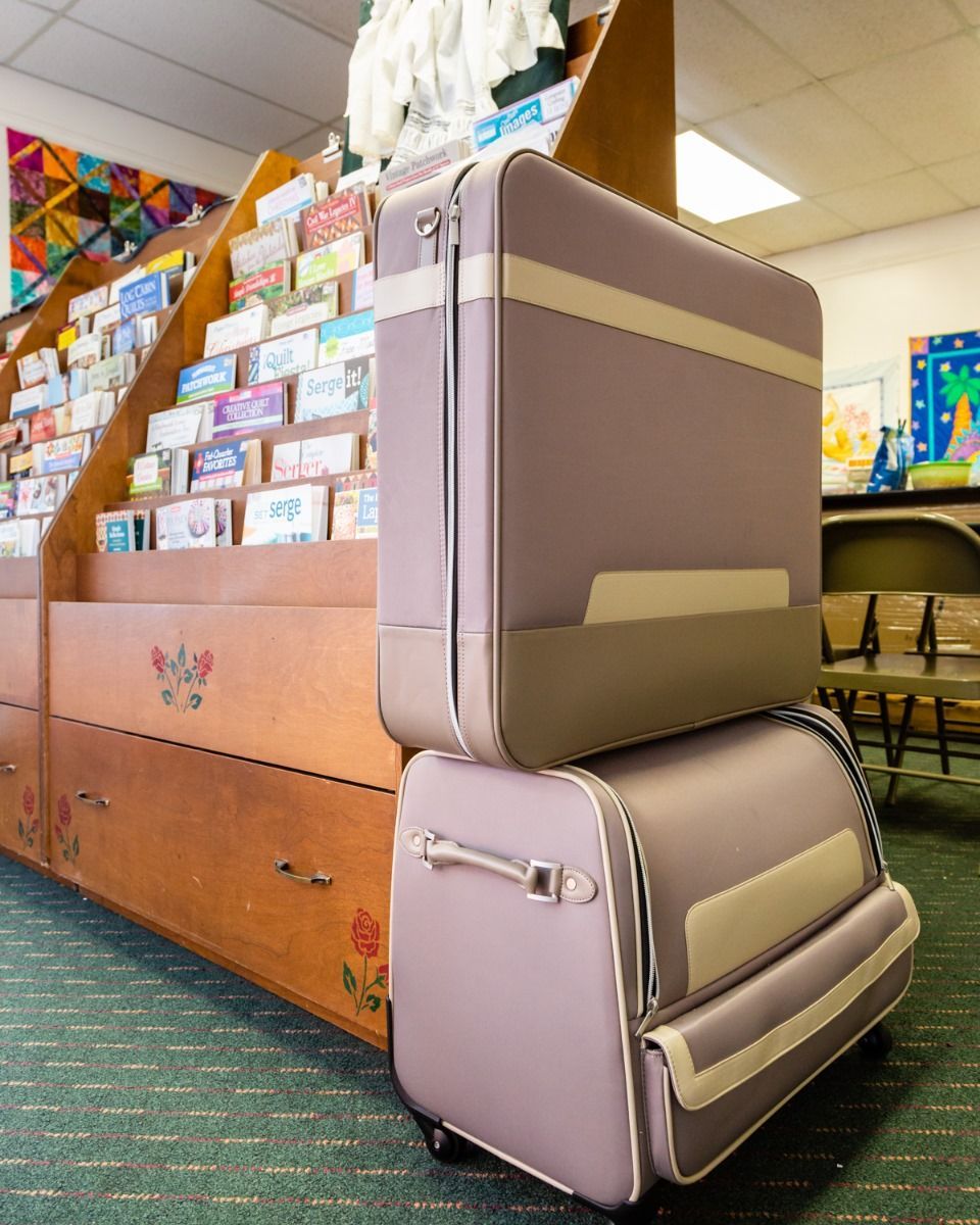 Stacked lavender and beige luggage beside a classroom bookshelf or display area.