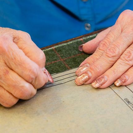 Hands cutting fabric with a ruler and rotary cutter on a sewing mat