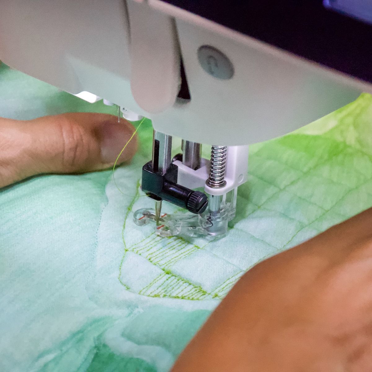 Close-up of a sewing machine stitching green quilted fabric with hands guiding it