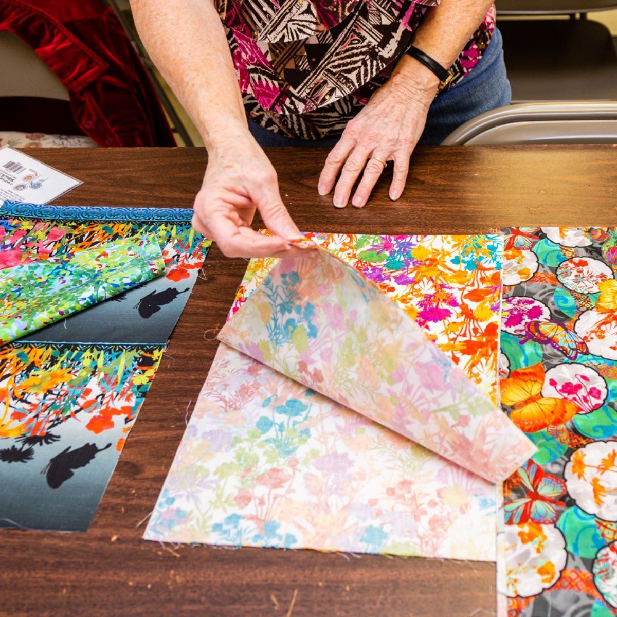 Hands lifting patterned paper samples on a table with colorful print swatches