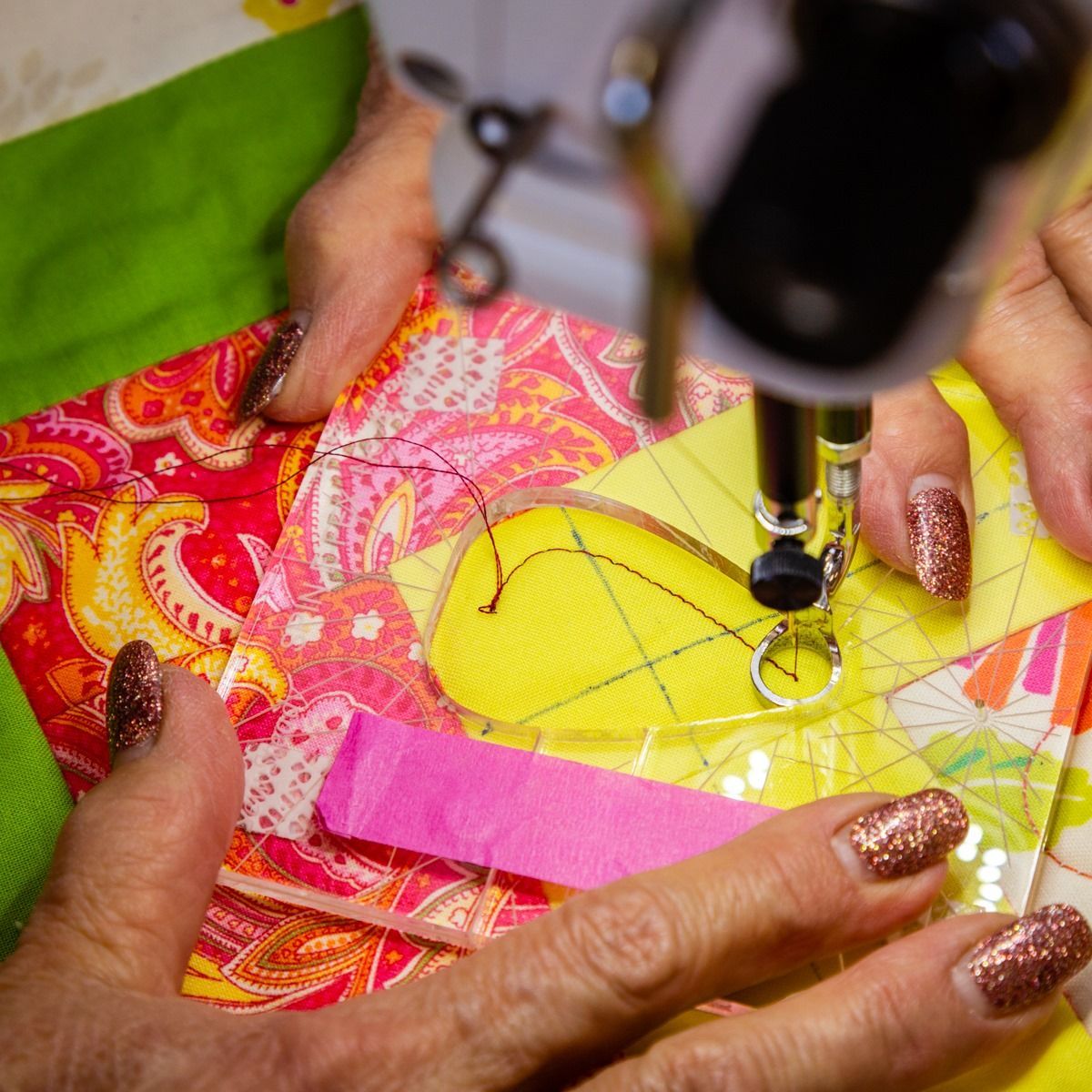 Hands sewing a bright pink and yellow quilt with a sewing machine.