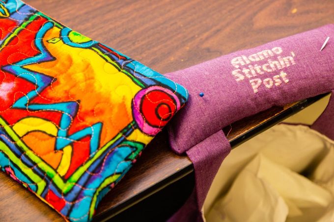 Colorful painted wooden toy fish on a bench with a purple cloth labeled “… Fishin’ Post”