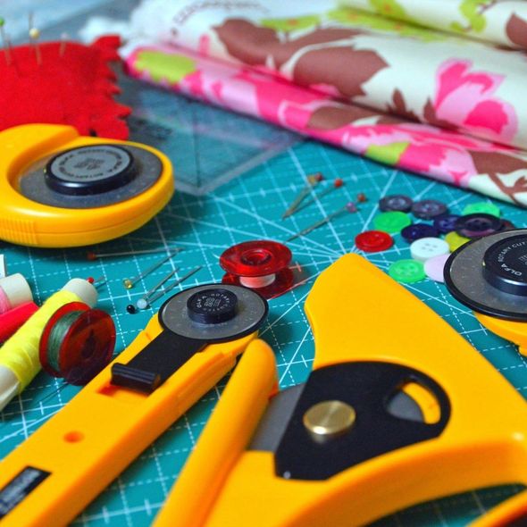 Sewing tools on a cutting mat: rotary cutters, pins, buttons, and folded fabric in bright colors