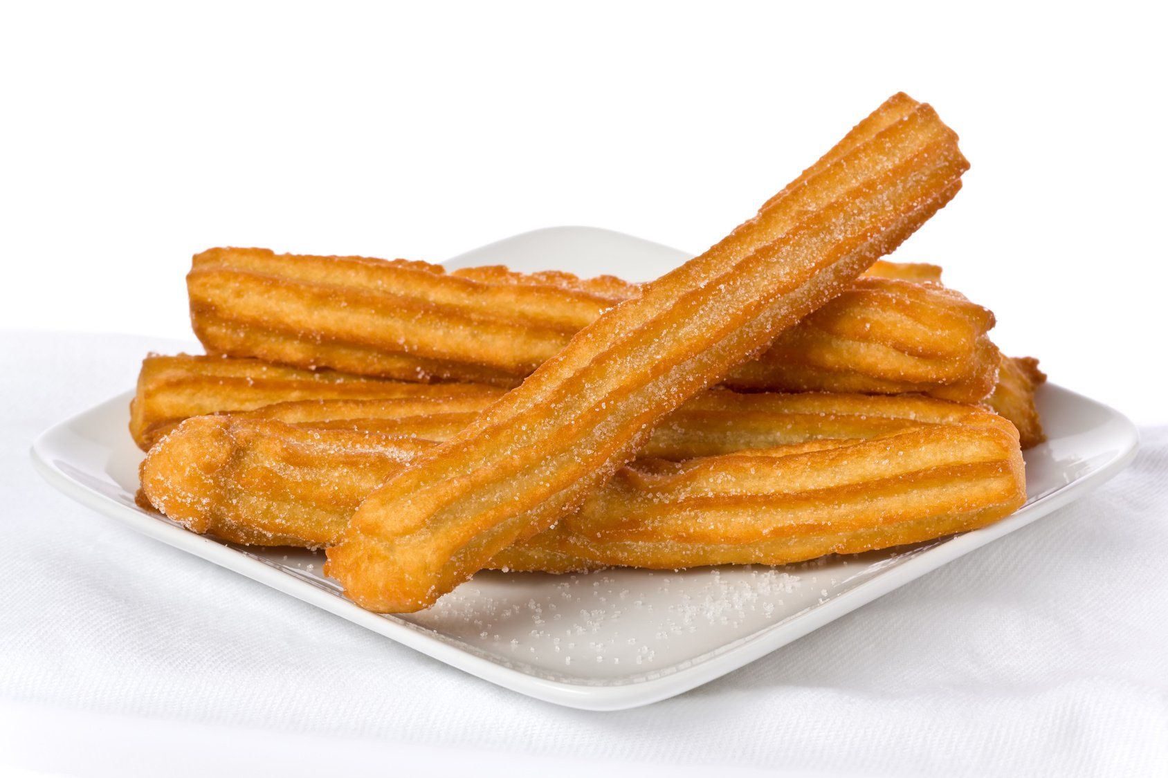 Churros, golden brown and sugared, on a white square plate.