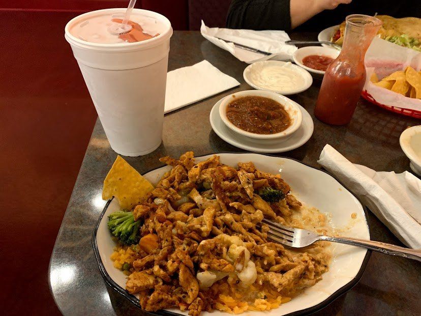 Plate of food with chicken and rice, drink, salsa, and tortilla chips on a restaurant table.