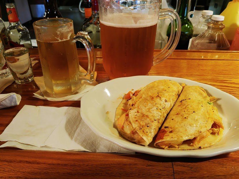 Two beers and a quesadilla on a wooden bar top.