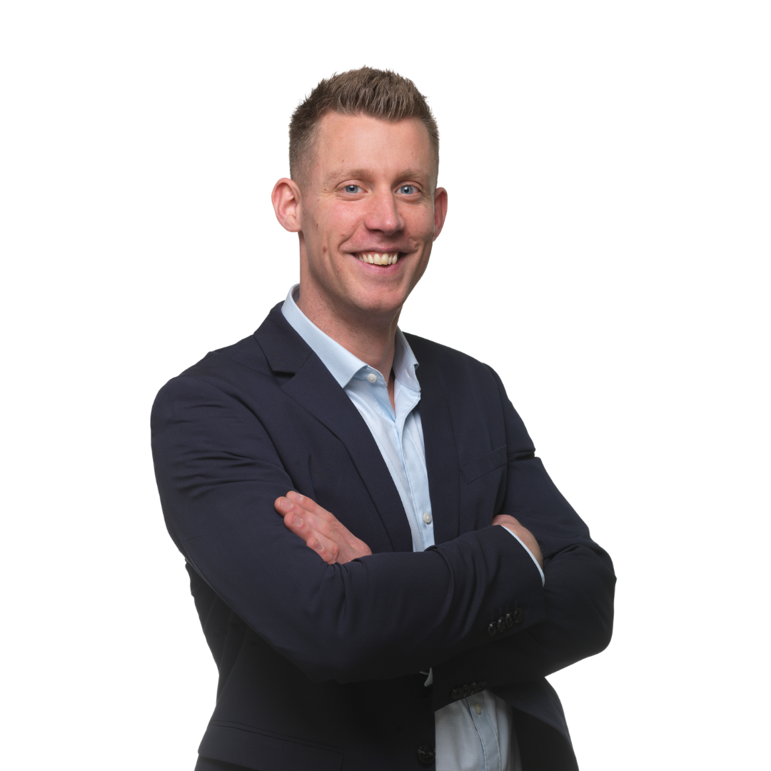 Een man met gekruiste armen, glimlachend, gekleed in een blauwe blazer en een lichtblauw overhemd.