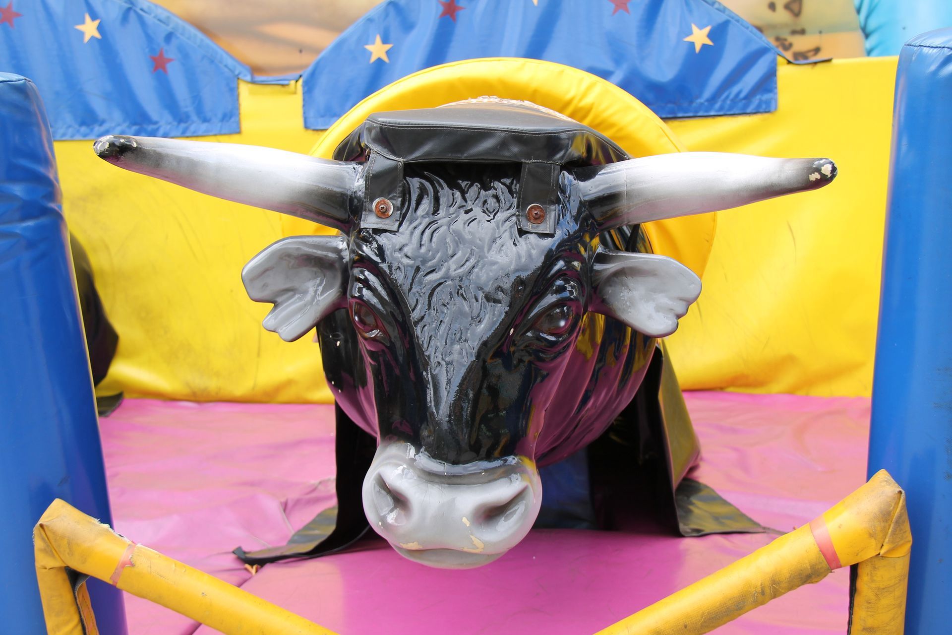 A mechanical bull is sitting in a fenced in area.