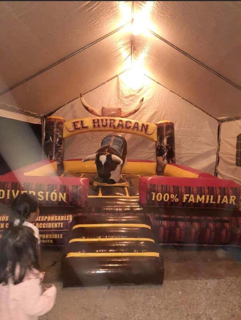 A man is riding a bull under a tent that says el huracan