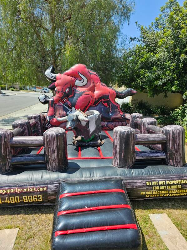 A large inflatable bull riding ride is sitting on top of a lush green field.
