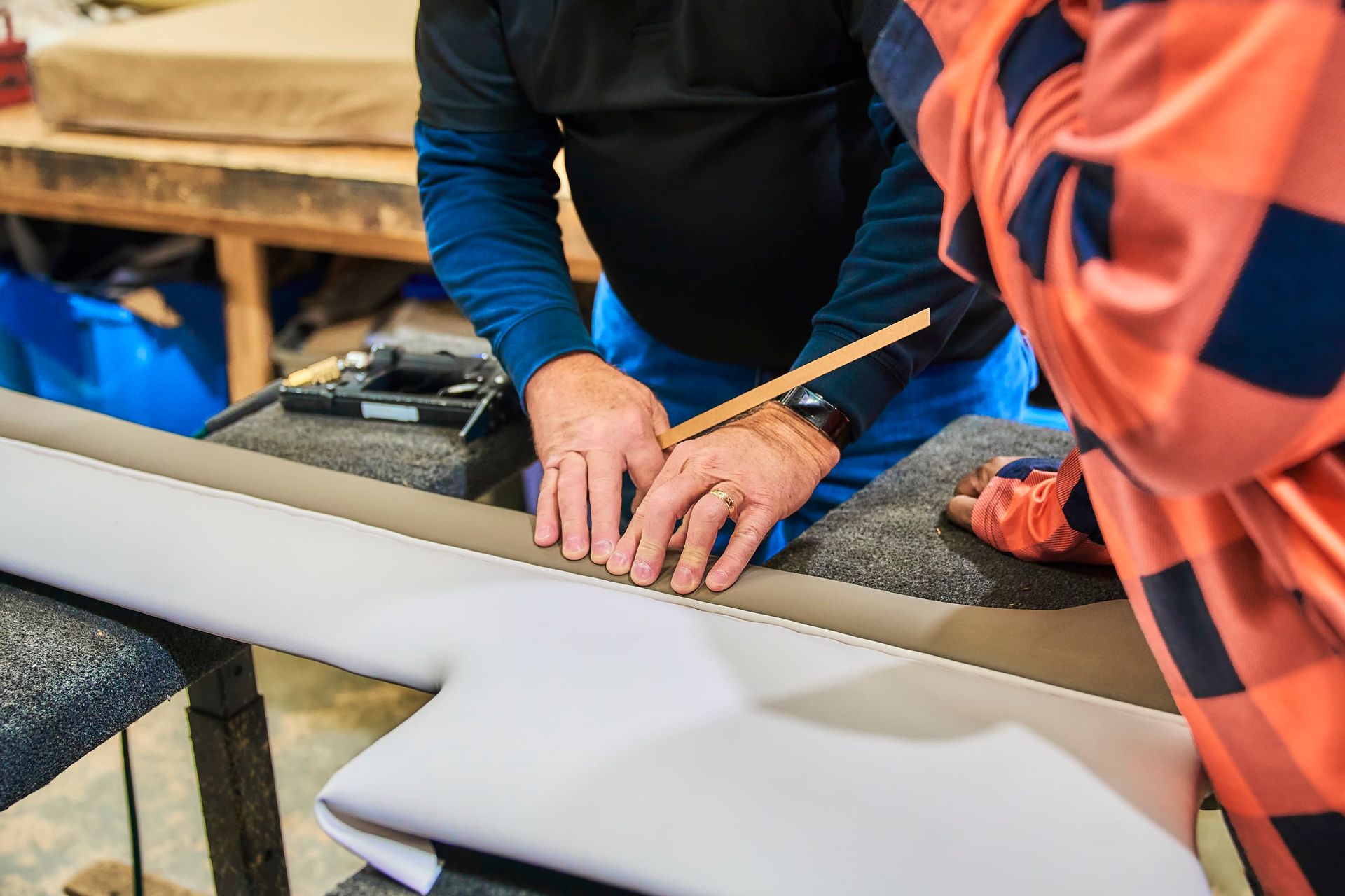 Person using a ruler to measure fabric on a work surface, another person in view.