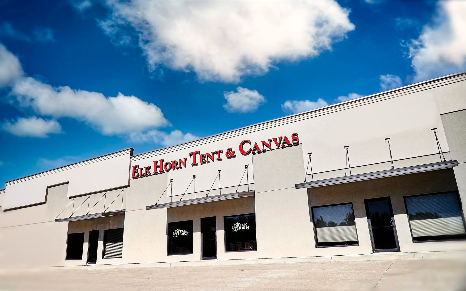 Elk Horn Tent & Canvas storefront, white building, red signage, blue sky, clouds.