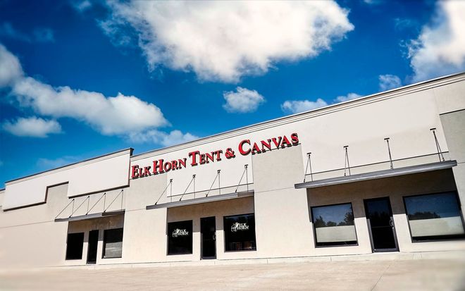 Elk Horn Tent & Canvas storefront, white building, red signage, blue sky, clouds.