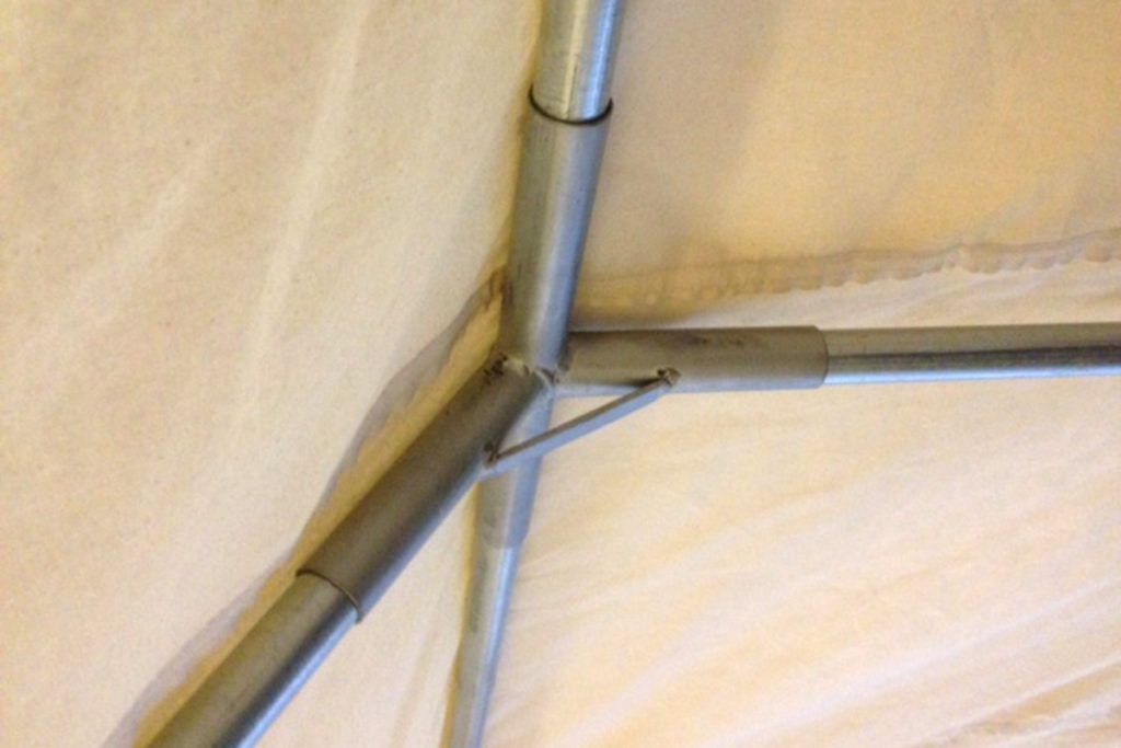 Metal tent frame joint, connected with metal pipes and brackets, fabric background.