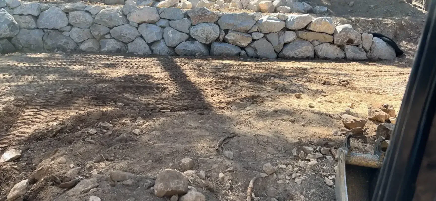 A stone wall is being built in the middle of a dirt field.
