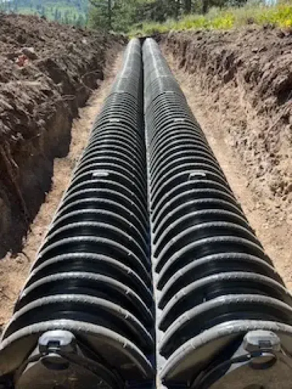 Two drain pipes are being installed in a trench.