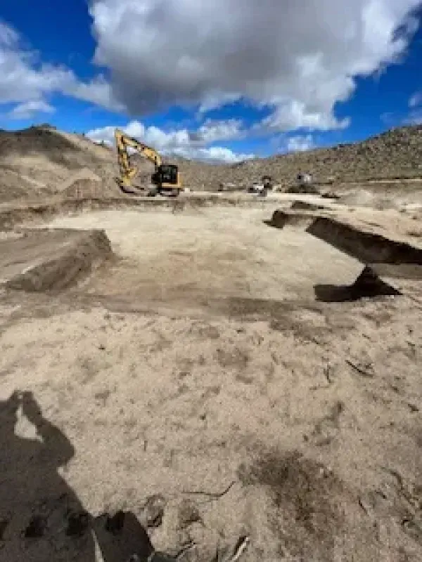 A large yellow excavator is sitting in the middle of a dirt field.