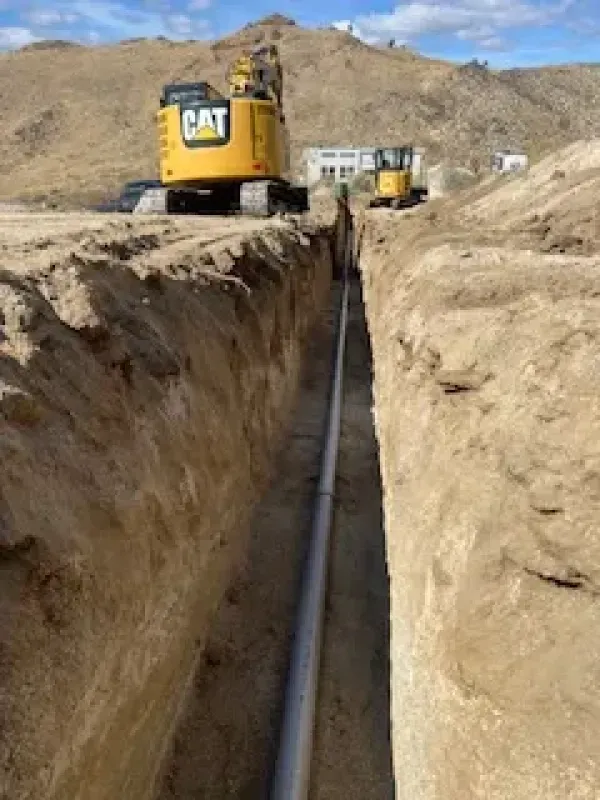 A cat excavator is digging a trench with a pipe in it.