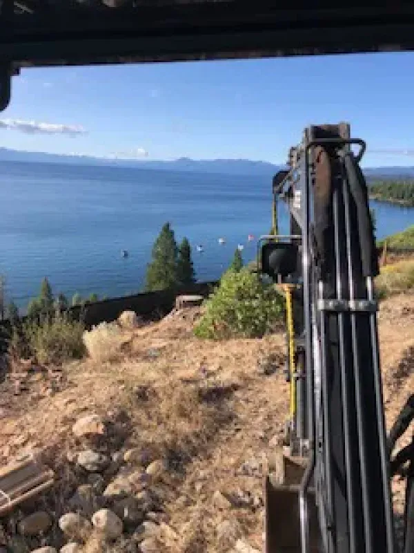 A large excavator is sitting on top of a hill overlooking a lake.
