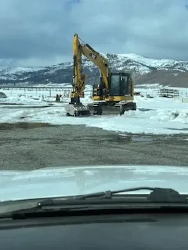 A yellow excavator is sitting on top of a snow covered field.