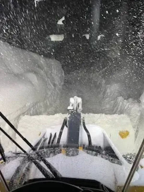A snow blower is blowing snow from the windshield of a vehicle.