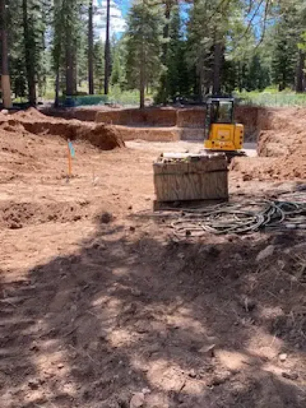 A yellow excavator is digging a hole in the dirt in the woods.