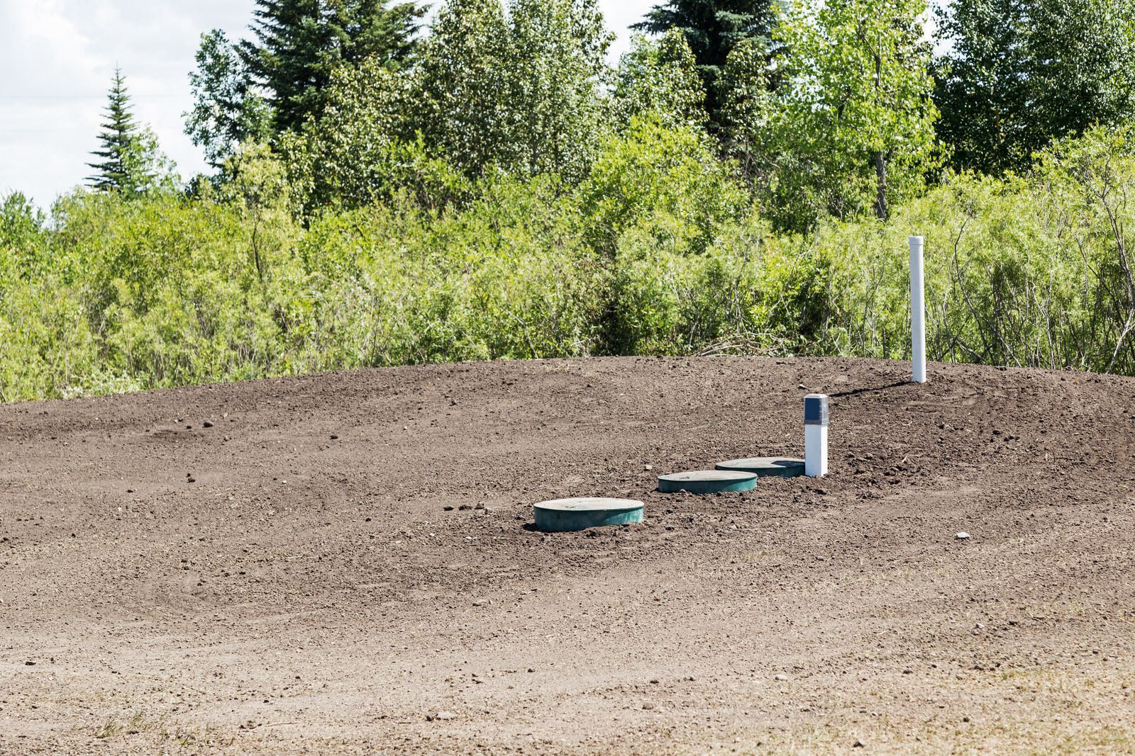 A row of septic tanks in a field with trees in the background.