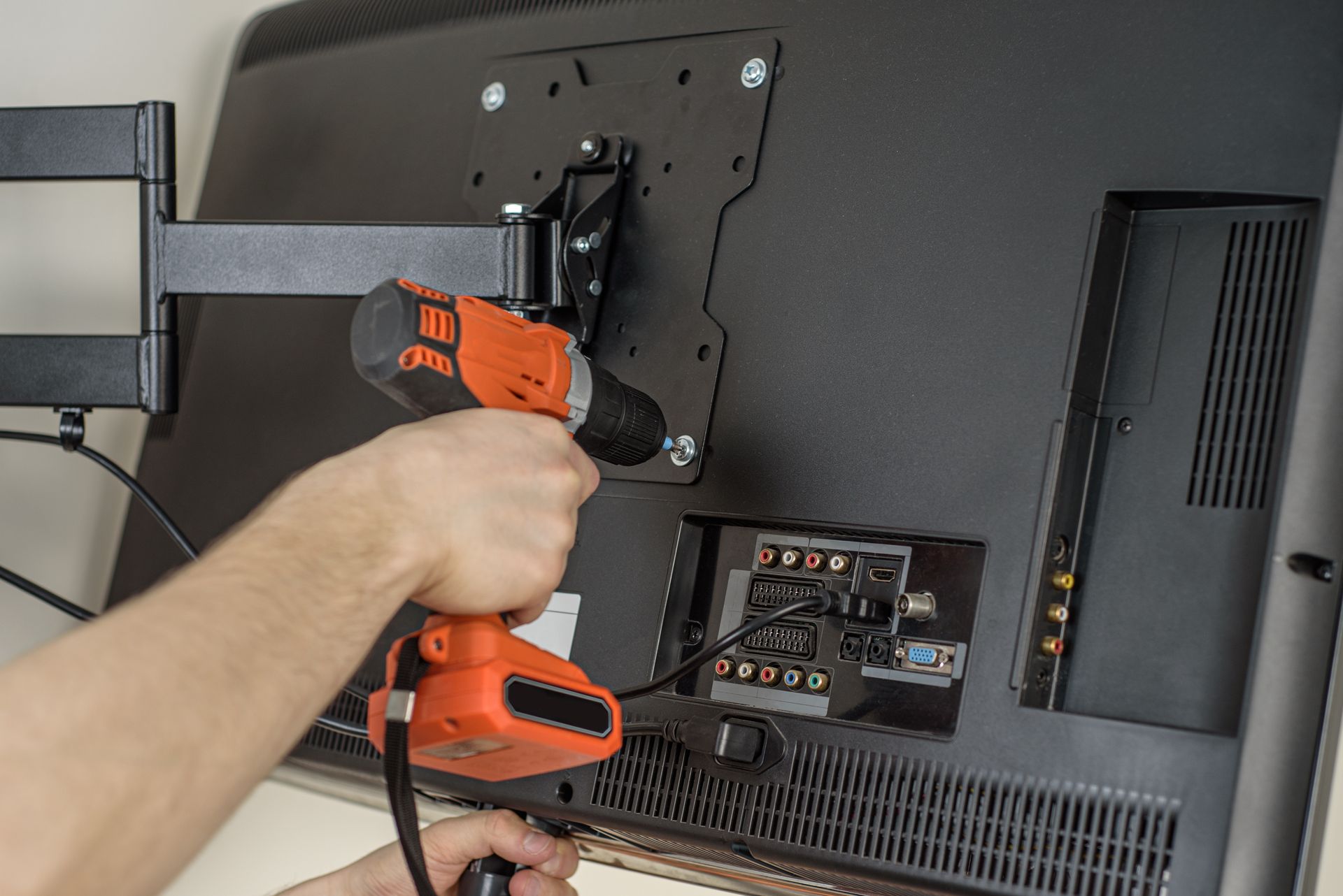 A person is using a drill to install a flat screen tv.