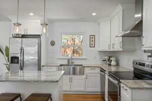 A kitchen with white cabinets , stainless steel appliances , granite counter tops and a sink.