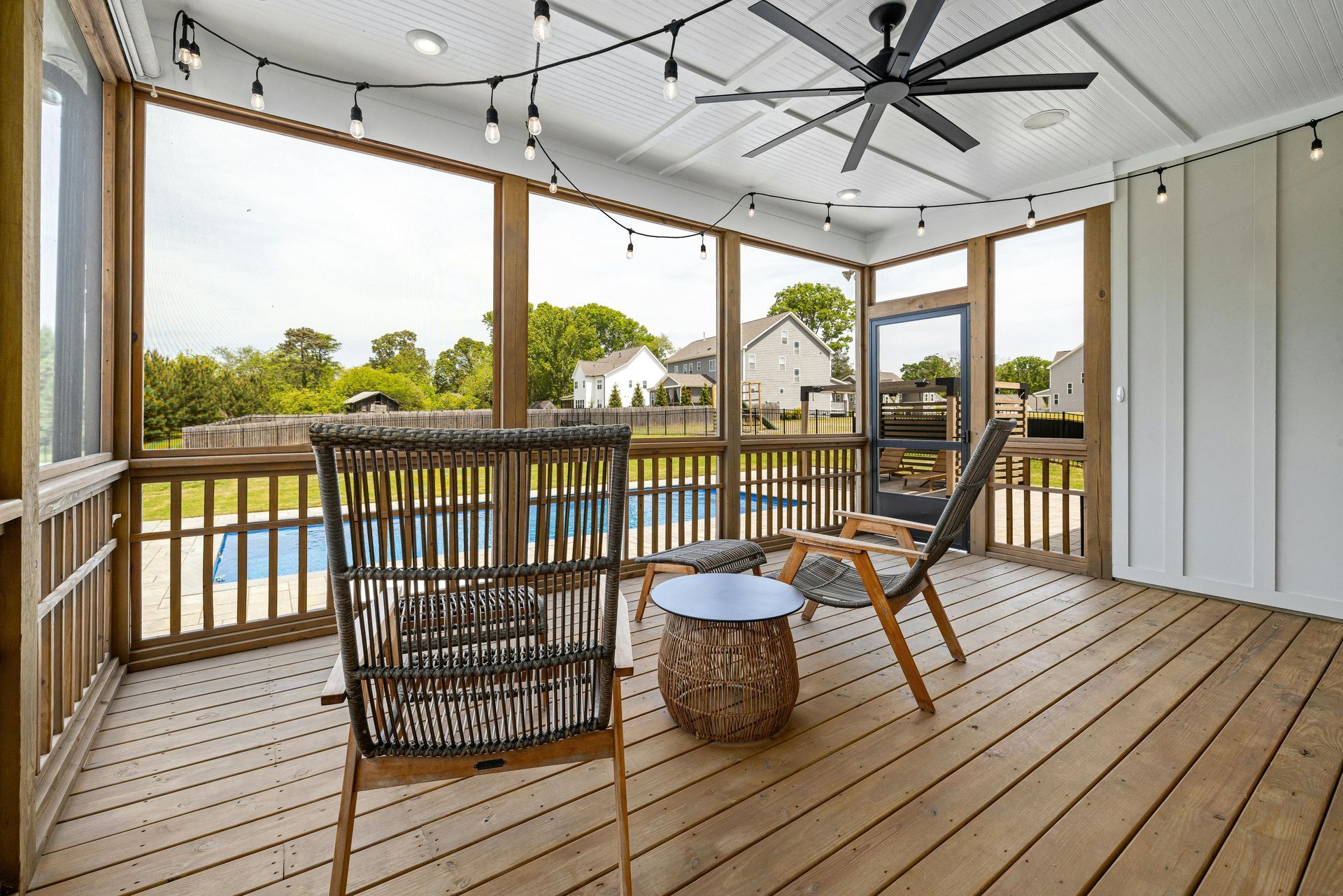 A screened in porch with chairs , a table and a ceiling fan.