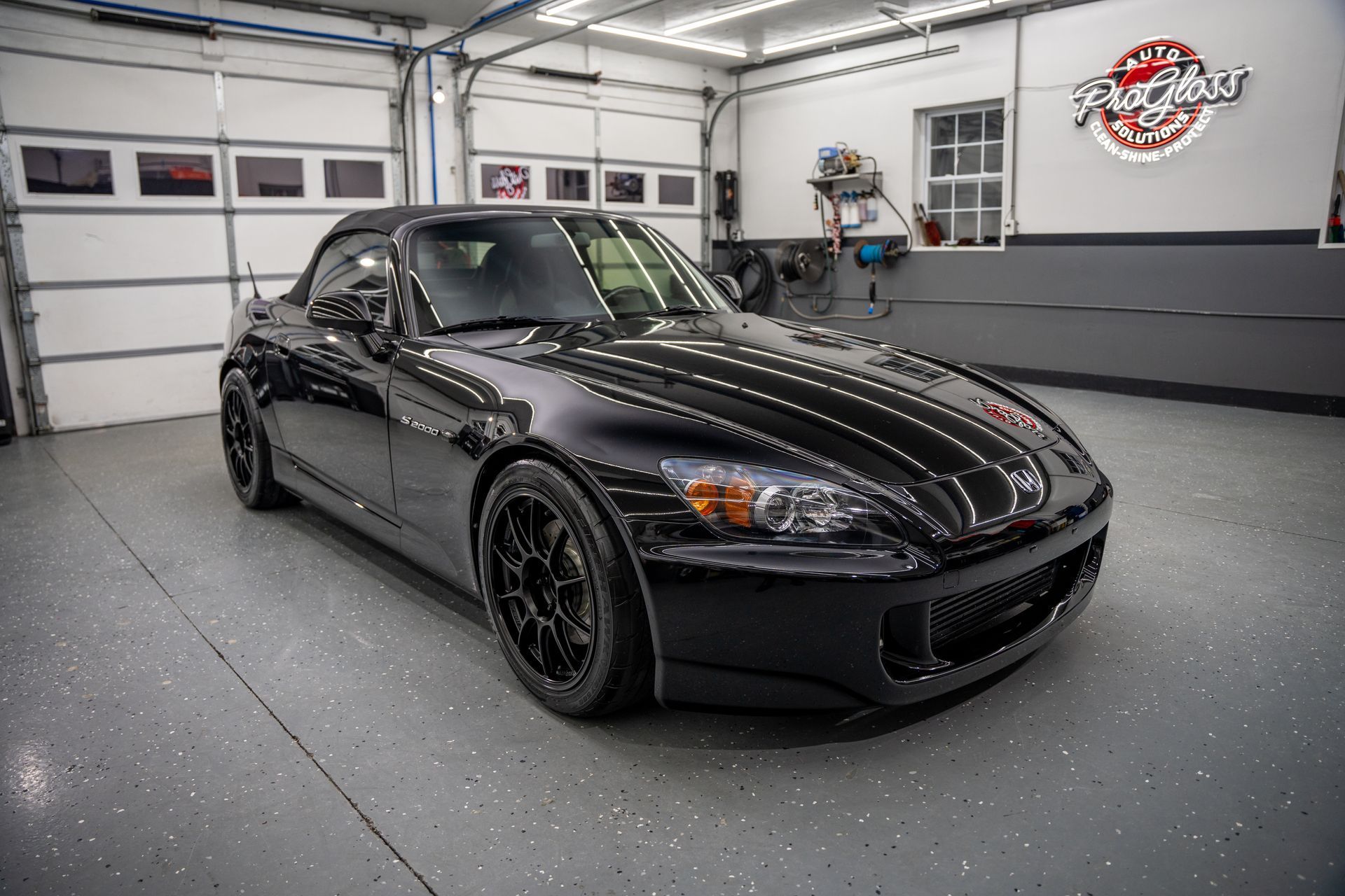 Black Honda S2000 convertible in a garage with a gray epoxy floor.
